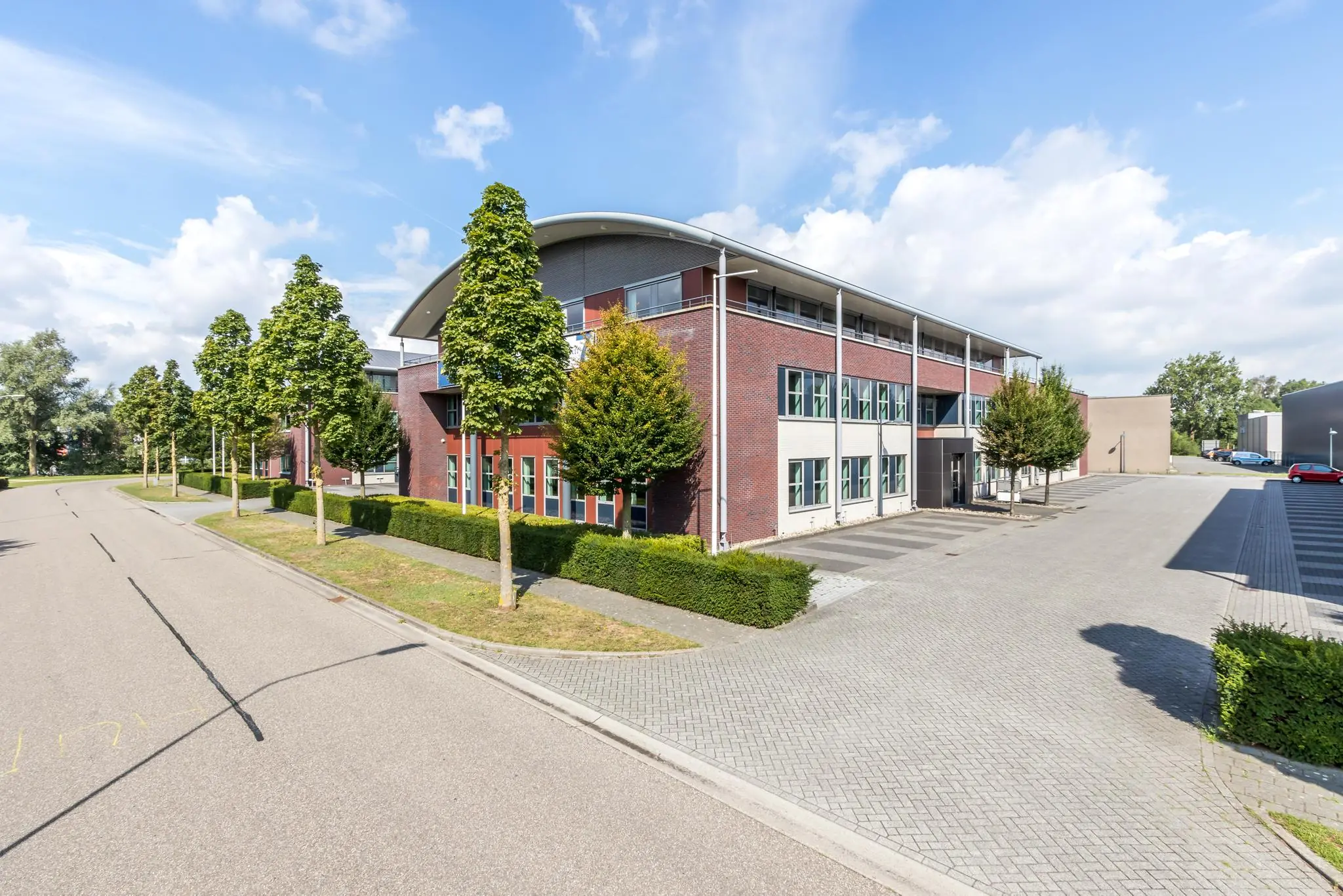 Modern kantoorgebouw aan de straat De Wel met omliggend groen en parkeerplaatsen.